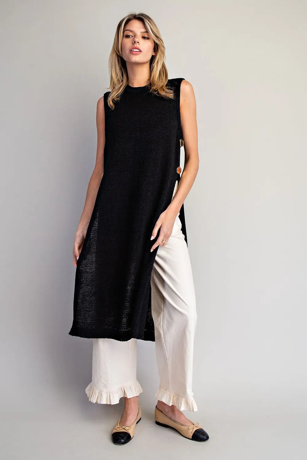 Woman wearing a black sleeveless top and white pants on a plain background