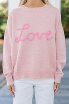 Women’s pink LOVE graphic knit sweater with relaxed fit, round neckline, and dropped shoulders