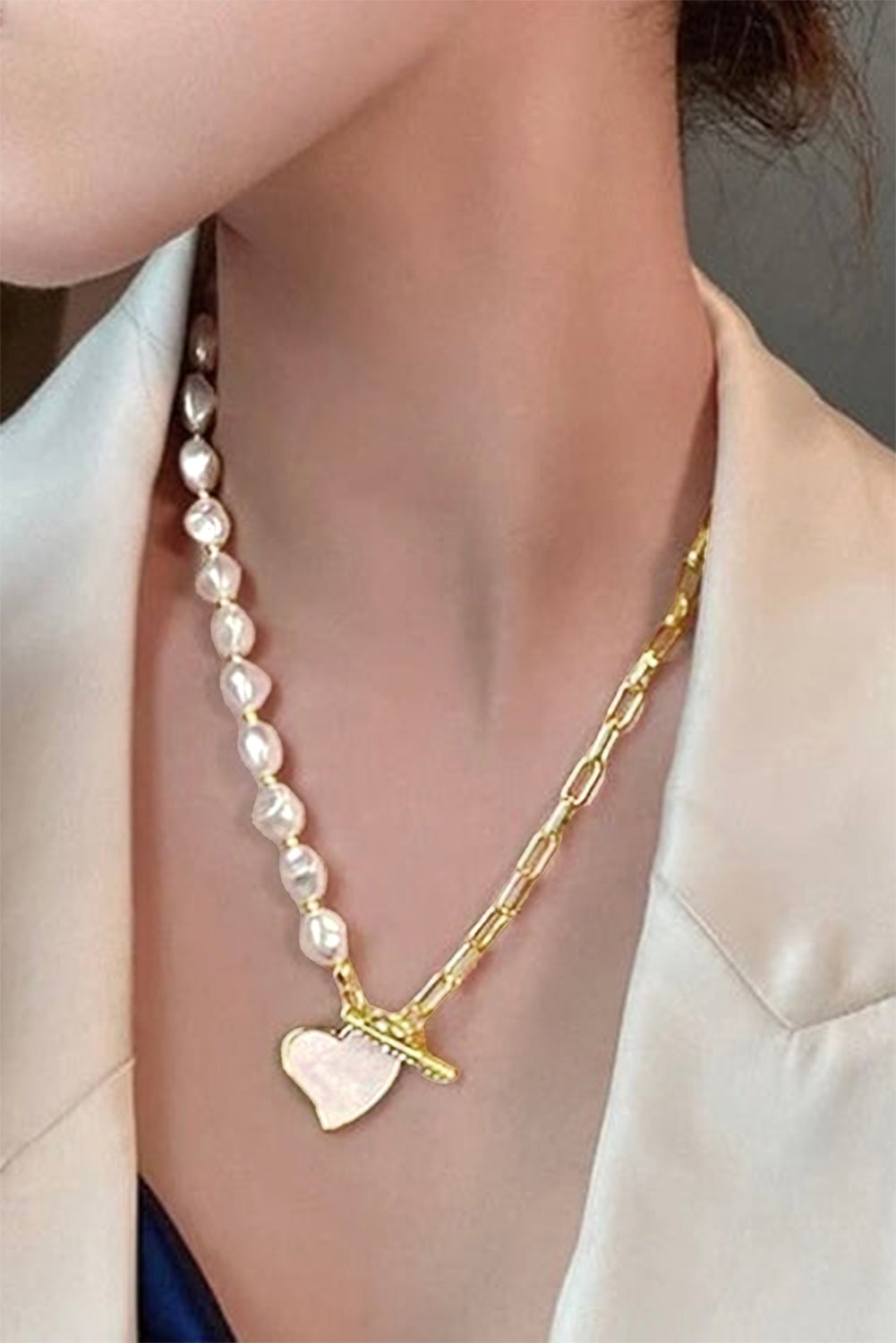 Necklace with heart pendant and pearl beads worn by a person in a white blazer.