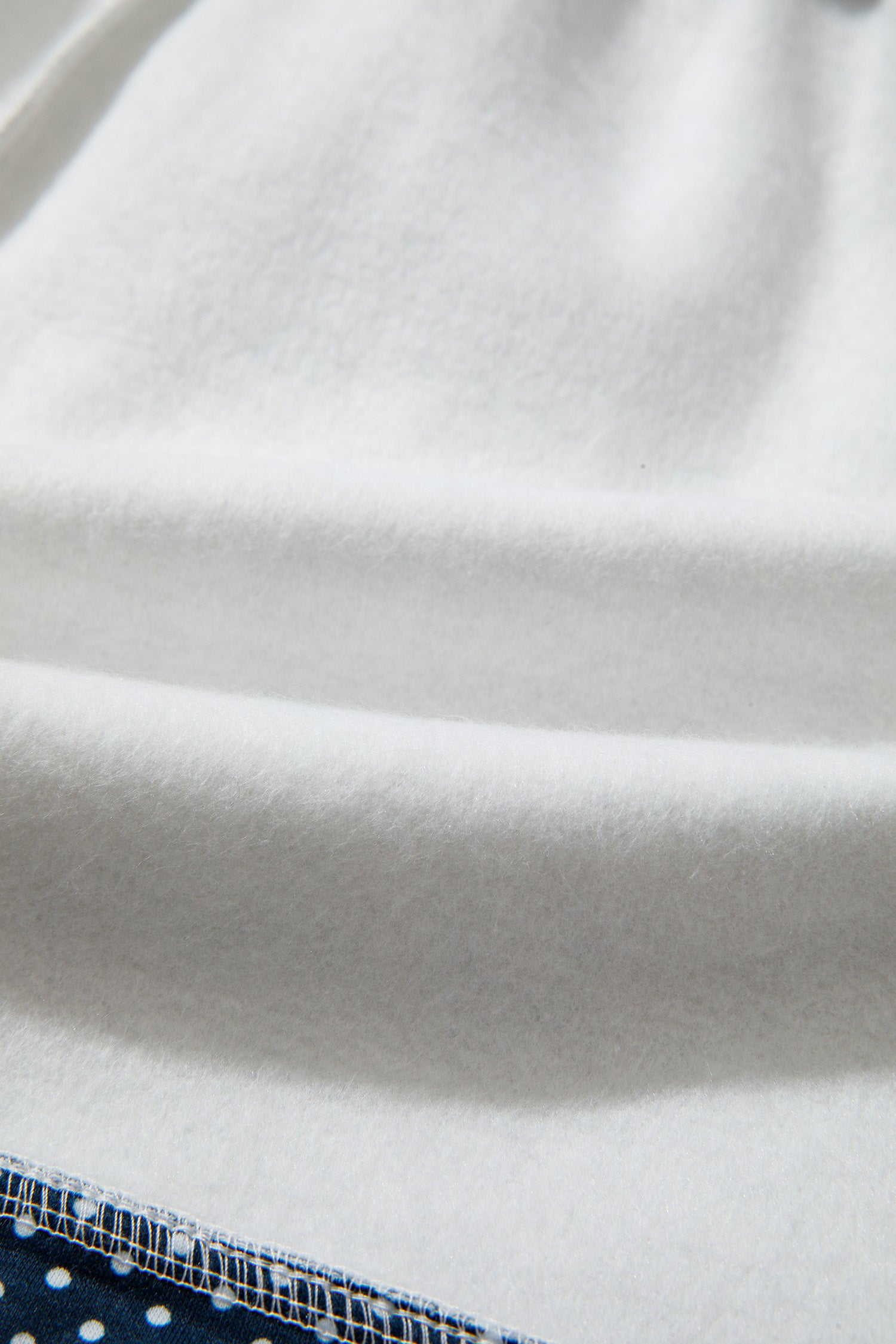 A close-up of a white textured fabric, likely fleece or sherpa, with soft folds and a small portion of a blue patterned textile visible at the bottom edge.