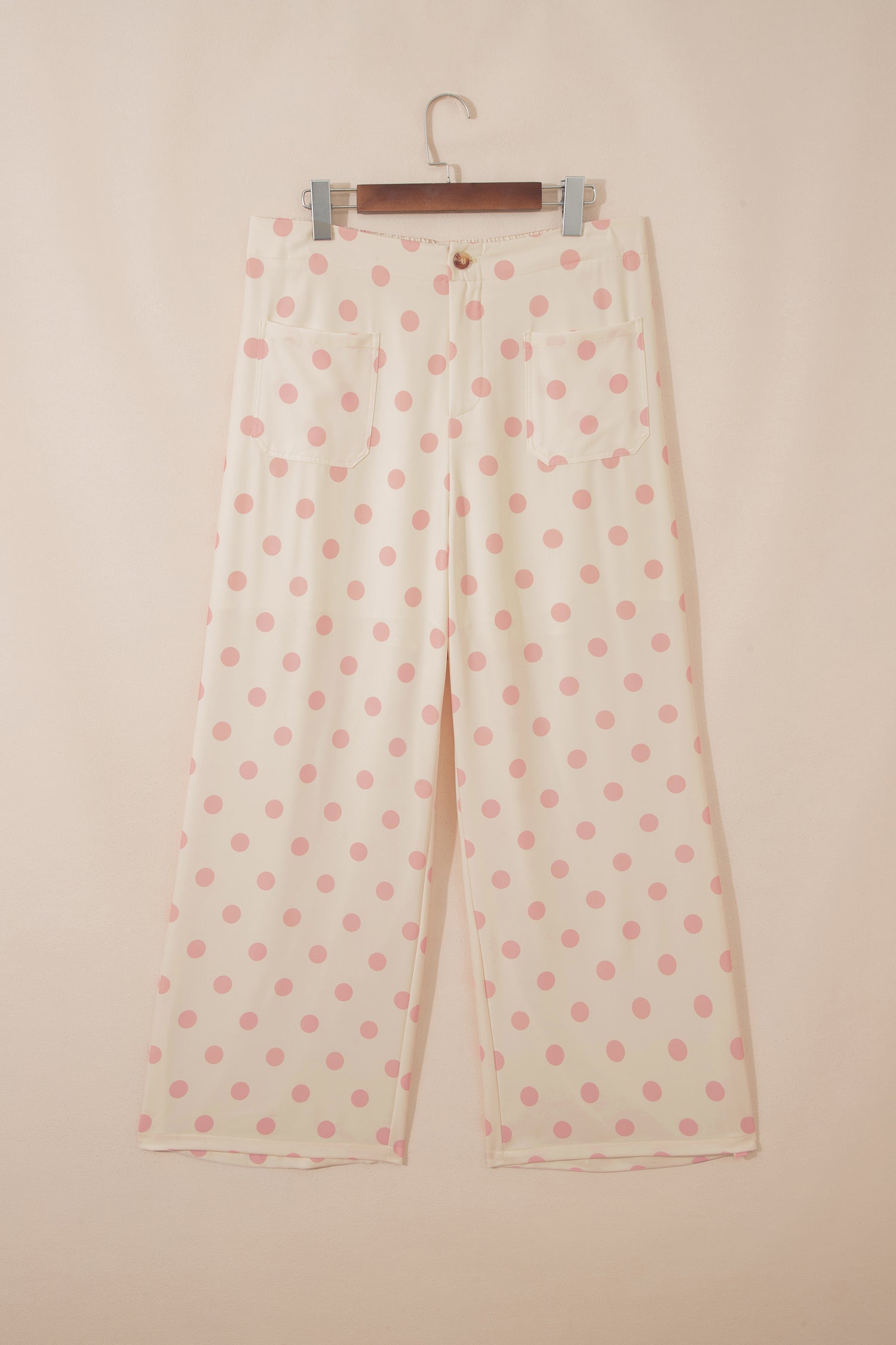 Polka dot pants on a hanger against a beige background