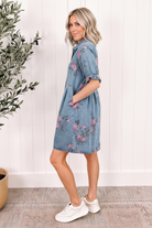 Sky blue floral denim shirt dress 3/4 back view showing ruffled cuff sleeves, A-line shift silhouette, and all-over pink rose print on enzyme-washed denim