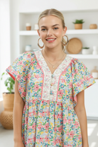 Close-up of blonde model wearing Umgee blue mix floral tiered mini dress showing V-neckline, contrast lace placket, pink trim and ruffle sleeves 