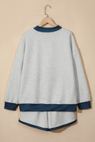 A light gray knit lounge set consisting of a long-sleeve top and matching shorts, hanging on a wooden hanger against a solid beige background. The top and shorts feature contrasting dark blue and white polka dot trim at the collar, cuffs, hem, and bottom of the shorts.