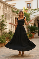 Black smocked ruffle top and maxi skirt two-piece set in motion, skirt swirling, showing lightweight breathable fabric and drawstring waist detail