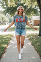 USA camo graphic tee knotted hem styled with denim cutoffs — candid walking lifestyle shot