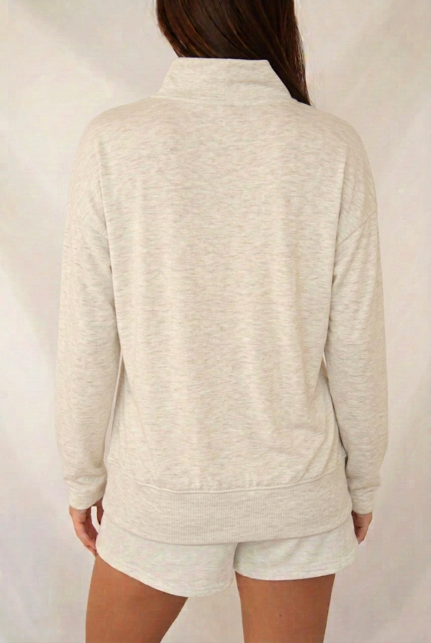 Back view of cream-gray mélange mock-neck long sleeve tee with a plain back, roomy relaxed fit, and ribbed cuffed bottom hem.