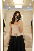 Oatmeal ribbed peplum tank mirror selfie — square neck, raw-edge detail, pleated hem, styled with black midi skirt in boutique fitting room