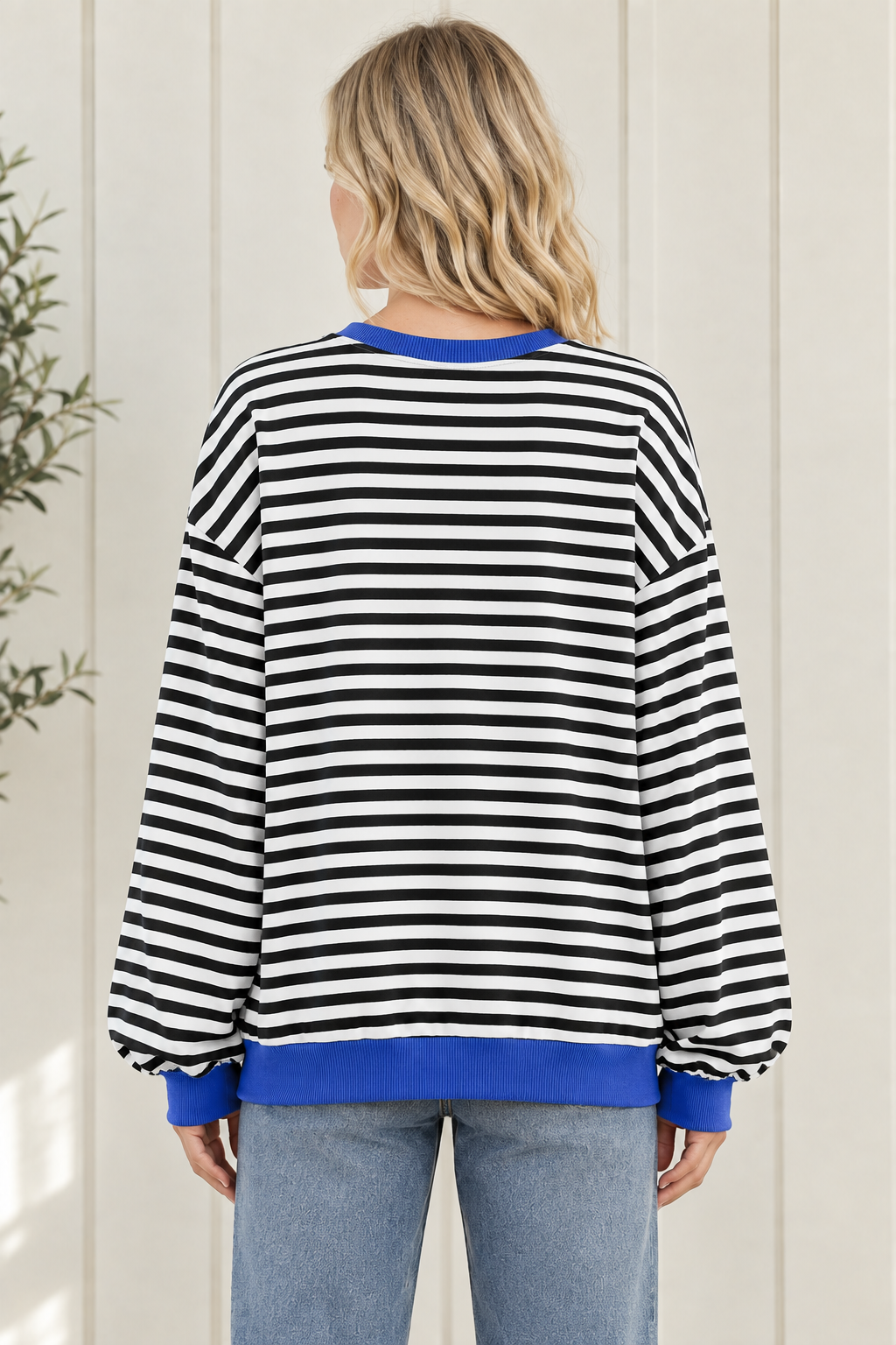 Back view of women's black and white striped sweatshirt showing oversized fit, long sleeves and blue ribbed hem.