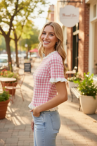 Pink gingham knit top side angle view showing scalloped ruffle neckline and ruffled sleeve detail, styled with light wash denim