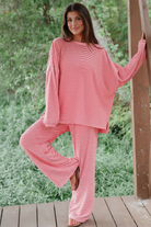 Model wearing red white stripe oversized drop shoulder pullover and wide-leg pants - front pose leaning on wooden post outdoors