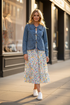 Quilted denim jacket with oversized ruffled collar and tie-front bows — front view, styled with floral midi skirt and white sneakers on urban street