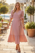 Red and white stripe wrap midi dress with puff tie sleeves, ruffle cuffs, V-neckline, and tiered flowy skirt styled with tan strappy sandals on sunny outdoor patio, boutique women's dress at Thread Bar Boutique
