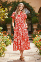 Red and cream bold paisley floral midi dress with pockets full body front view, hands in pockets, flutter sleeves, smocked waist, ruffle hem, outdoor lifestyle