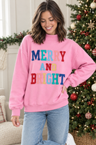 Angled view of pink Merry and Bright holiday pullover styled with light wash jeans