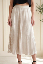 Detail of cream silver metallic midi skirt showing fine vertical pleats and a broad smooth elastic waistband.