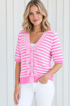 Angled front view of pink striped V-neck knit sweater with three bow ties, styled with white jeans