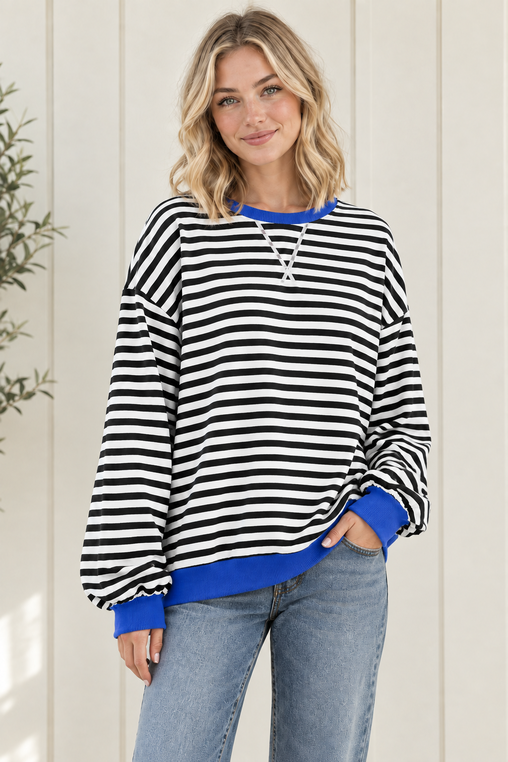 Three quarter view of oversized striped pullover sweatshirt with blue neckline, cuffs and hem, styled with jeans.