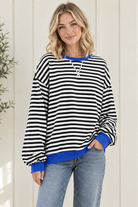 Three quarter view of oversized striped pullover sweatshirt with blue neckline, cuffs and hem, styled with jeans.