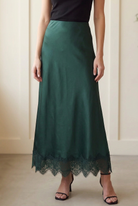 Detail of forest green woven satin maxi skirt showing the lustrous fabric and scalloped floral lace trim.