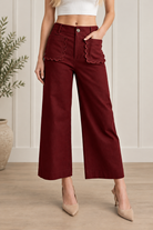 Front view of burgundy cropped wide leg pants showing scalloped patch pockets, a button waist and belt loops.