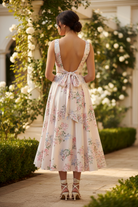 Back view of blush floral midi dress showing open back with self-tie bow closure, wide shoulder straps, and full A-line pleated skirt falling to ankle