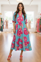 Blue aqua floral print contrast trim midi dress full-length front view — brunette model boutique interior natural window light coral heeled mules