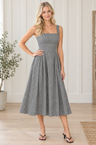 Black and white gingham square neck midi dress with defined waist and pleated skirt, hand on hip view