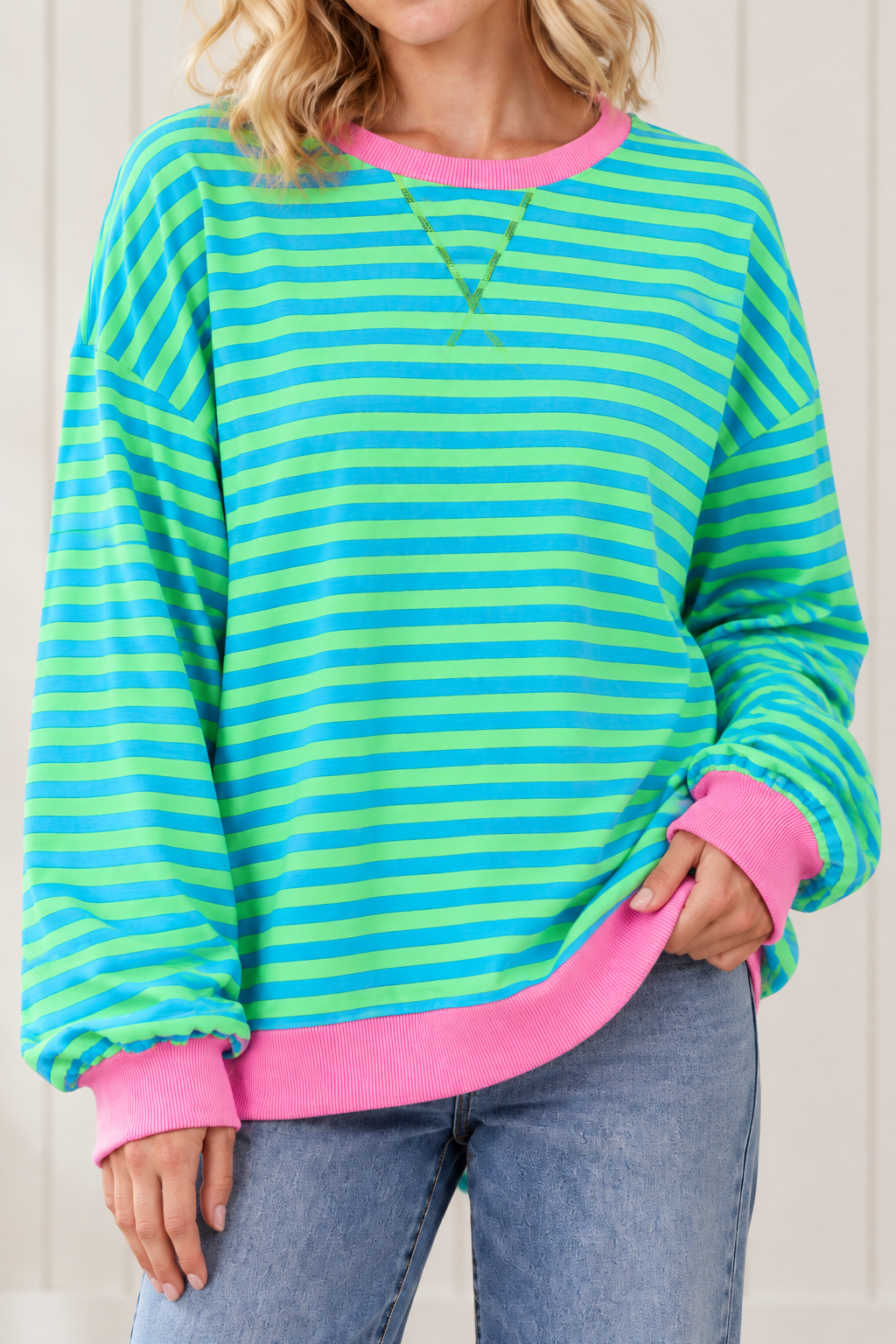 Close-up of blue and green striped pullover highlighting front V stitching, pink ribbed neckline and cuffs.