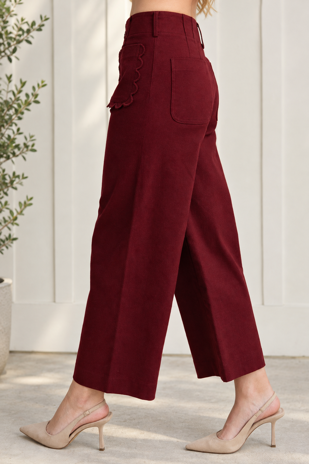 Side and rear view of burgundy cropped wide leg pants showing a plain back patch pocket and scalloped front pocket.