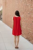 Back view of Umgee tomato red drop waist mini dress showing ruffle neckline and ruffle hem detail, brunette model on urban sidewalk