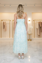 Back view of mint blue floral midi dress with adjustable spaghetti straps and smocked corset bodice, styled in a boutique setting