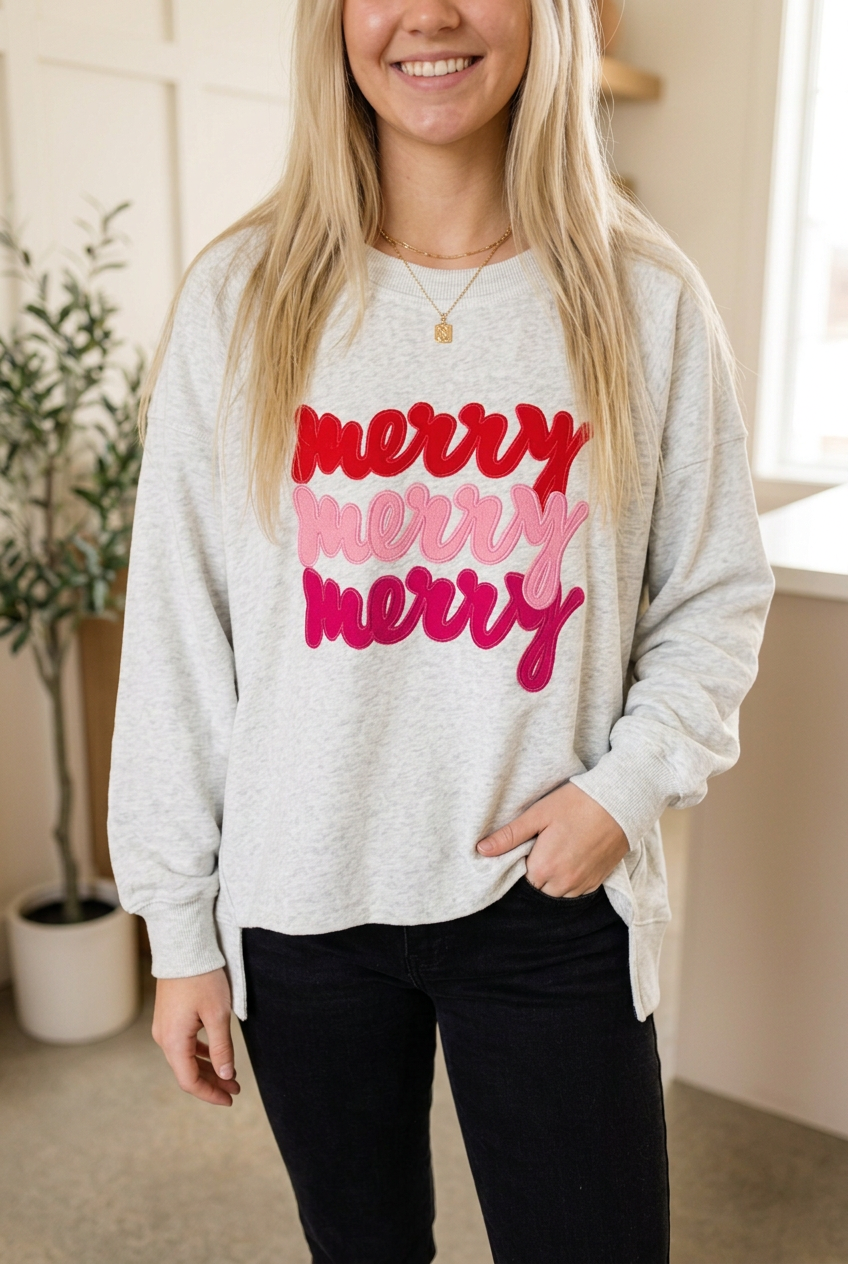 Light grey Merry sweatshirt with three stacked red and pink slogans, ribbed cuffs and a split side hem, styled with black jeans.