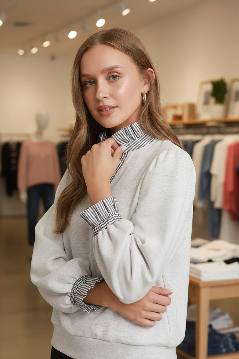 Close-up of a blonde woman wearing the Umgee heather white sweatshirt top showing the contrast navy and white vertical stripe ruffle collar and smocked ruffle stripe cuffs detail with gold hoop earrings