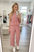 Blonde model taking mirror selfie in boutique dressing room wearing red white gingham peplum top and wide-leg trouser set