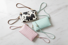 Flatlay of all three crossbody bags on marble surface - cow print, pink gingham, and mint gingham