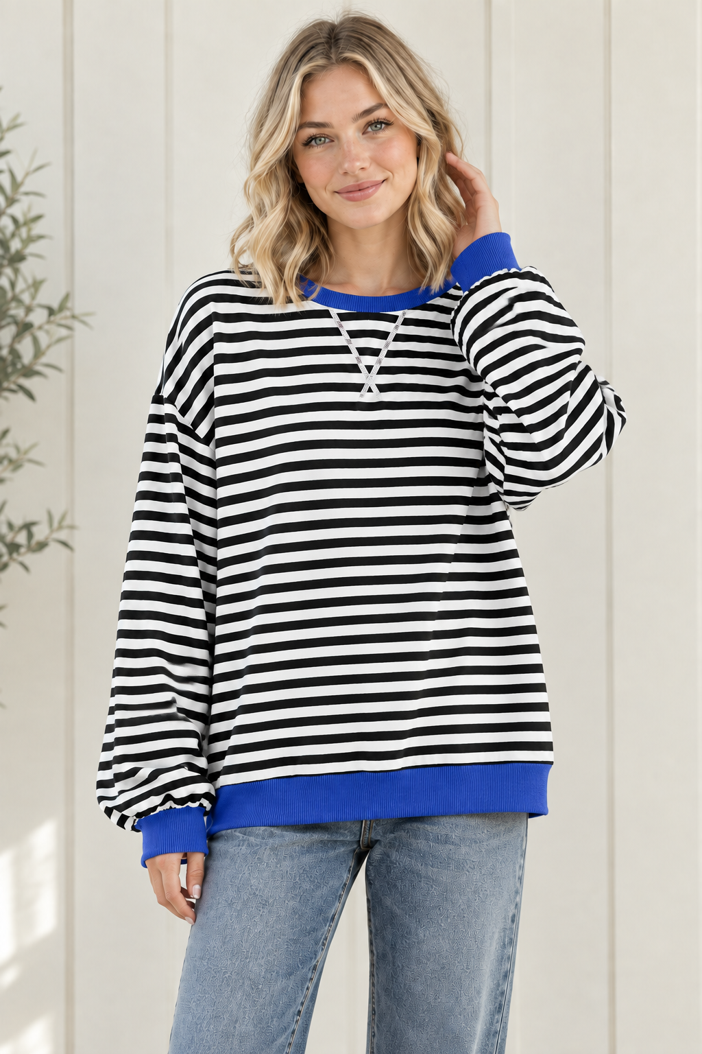 Women's oversized black and white striped sweatshirt with blue ribbed trim and drop shoulders, styled with jeans in a relaxed front pose.