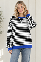 Women's oversized black and white striped sweatshirt with blue ribbed trim and drop shoulders, styled with jeans in a relaxed front pose.