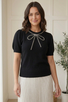 Close view of silver beading outlining the crew neckline and bow with long tails on a black half sleeve sweater.