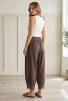 Rear three-quarter view of chocolate brown woven barrel pants with roomy curved legs, cropped length, and scalloped floral lace hems.