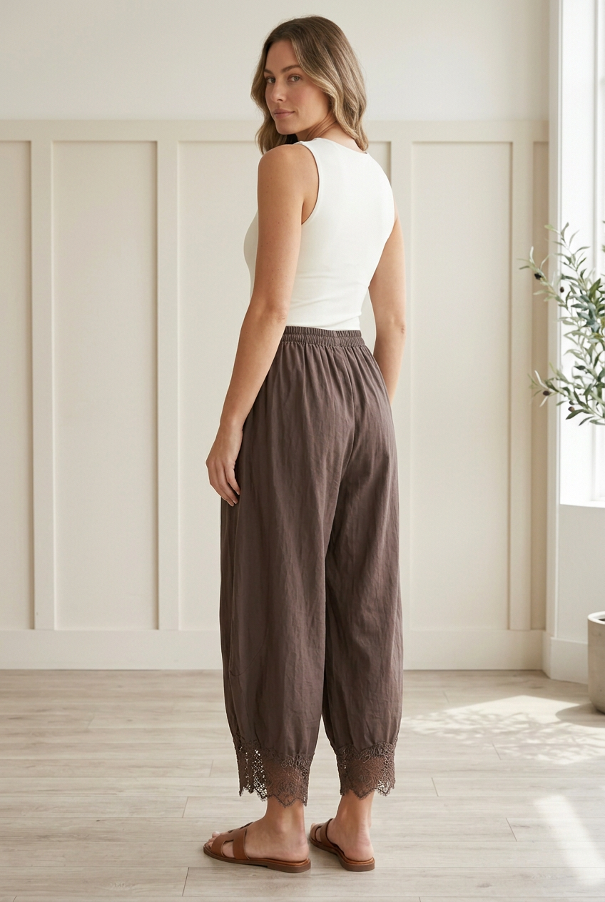 Rear three-quarter view of chocolate brown woven barrel pants with roomy curved legs, cropped length, and scalloped floral lace hems.