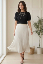 Black beaded bow sweater with an embellished crew neckline and puffed half sleeves, styled with a silver pleated skirt.