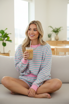 Blonde model seated on sofa with iced coffee wearing pink and mint stripe lounge set with pink ribbed collar and cuffs, lifestyle shot, Thread Bar Boutique