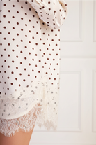 Close-up detail of ivory polka dot oversized shirt lace hem trim, showing delicate lace embellishment along the bottom hem
