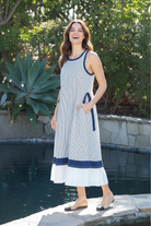 Brunette model laughing with hand in pocket wearing navy striped contrast hem maxi dress with white ruffle hem, poolside lifestyle shot