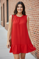 Close-up of ruffle trim neckline detail on Umgee tomato red sleeveless drop waist mini dress, worn by brunette model on urban sidewalk