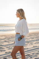 Light blue stripe elastic waist denim shorts three-quarter side view on beach, relaxed summer casual style