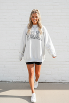 Oversized PRAY embroidered mock neck sweatshirt in heather gray, walking lifestyle shot, white stone wall, women's faith graphic sweatshirt