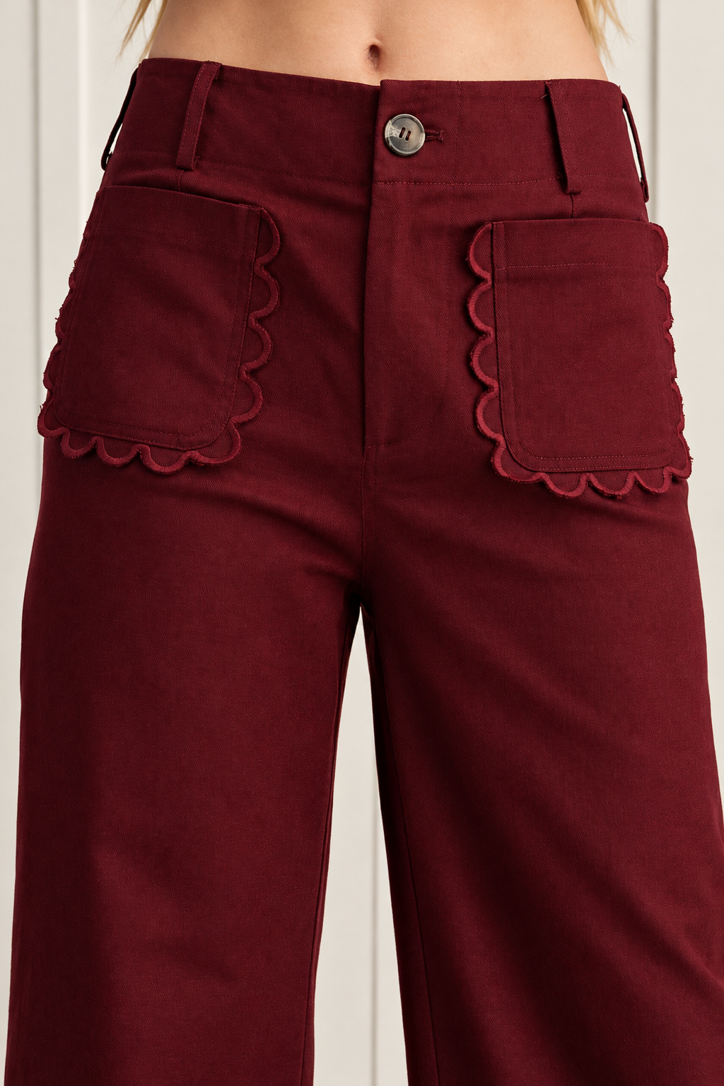 Burgundy high waisted pants detail showing two large front patch pockets with scalloped edges and visible stitching.