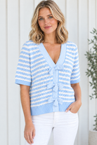 Angled front view of sky blue striped V-neck bow detail knit sweater styled with white jeans